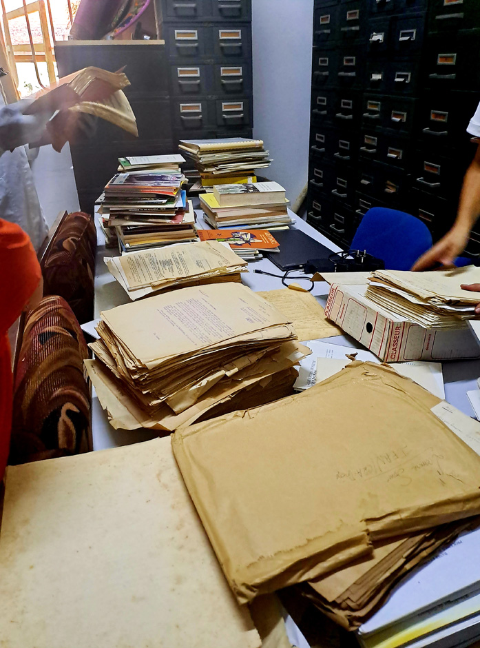 Photo d'archives (vieux papiers jaunis) étalées sur une table devant des armoires à archives